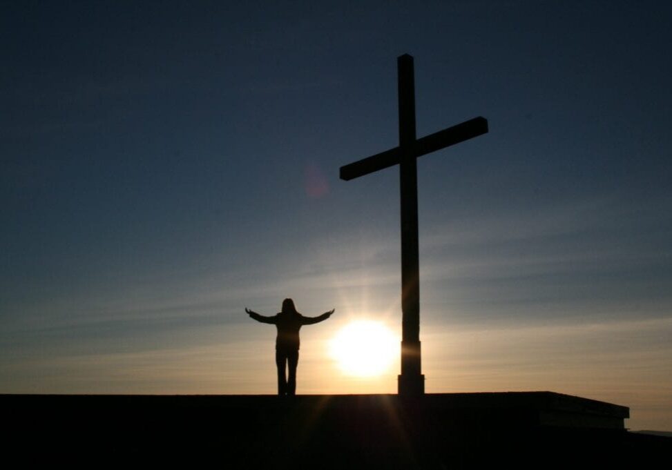 man praising and singing to the lord near the cross